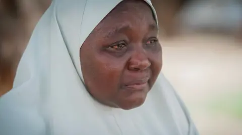 A woman wearing a white hijab, her eyes red from crying
