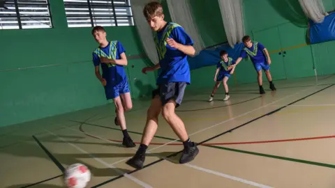 Furness Education Trust Four boys play football in the sports hall at Walney School.