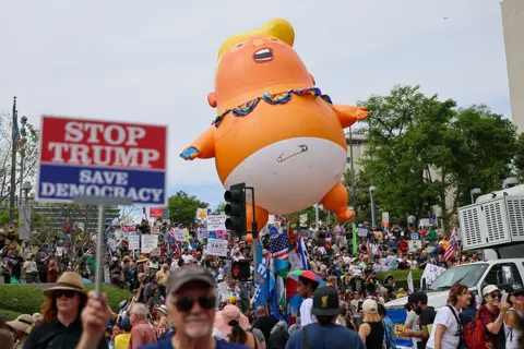 Getty Images Protestors are seen gathered, waving signs and a giant Trump inflatable that makes him appear as an infant wearing a diaper. 