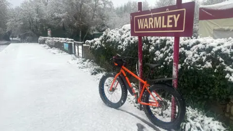 Luke Joy-Smith A mountain bike parked next to a sign saying Warmley, with snow on the ground and hedgerow