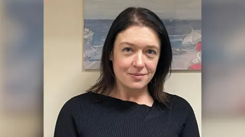 Wiltshire Police/PA Media Head and shoulders image of Joanne Young in a black top. She has black hair and is smiling. She is standing in a room in front of a painting.