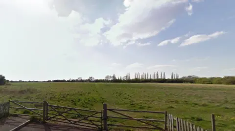 Google Gates in front of open fields, with trees in the distance and blue sky above.