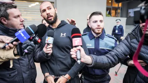 Getty Images Andrew Tate speaks to reporters as he leaves Romania's anti-organized crime and terrorism directorate.