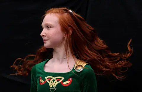 A young girl with red hair, wearing a green velvet Irish dancing outfit