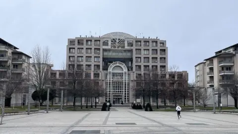 A grey building in the middle of a tree-lined square