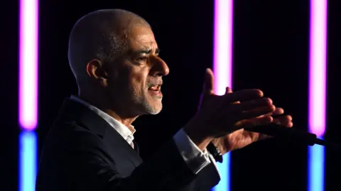 Mayor of London Sir Sadiq Khan delivers a speech during London Tech Week. He is pictured speaking into a microphone with his hands open either side of the microphone. 