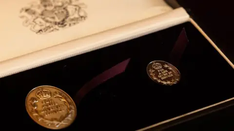 The picture shows two medals with the words for a life given in service in a case with a purple ribbon 