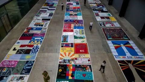 Reuters A shot taken from above as visitors view the UK AIDS Memorial Quilt, made of 42 quilts and 23 individual panels representing the 384 individuals who lost their lives to HIV and AIDS in the UK, displayed at Tate Modern, in London.