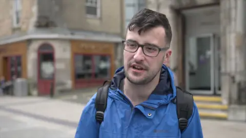 A man in a blue raincoat and glasses with dark hair