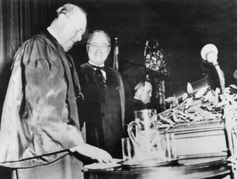 Getty Images Black and white photo of Sir Winston Churchill and US President Harry Truman standing at a lectern. Churchill is looking down at a piece of paper on a table and Truman is smiling at the camera