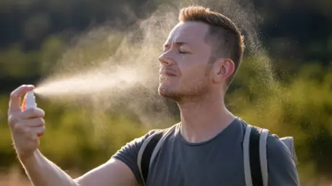 Portrait of man on hot summer day. Person applying face mist for refreshing.