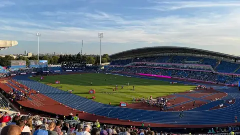 Chris Brown A photo of a stadium which is blue and orange with some pink. The grass in the middle is green.