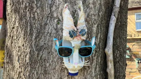 Shariqua Ahmed/BBC A white milk bottle that has been turned into a bunny. blue sunglasses have been placed on it.
