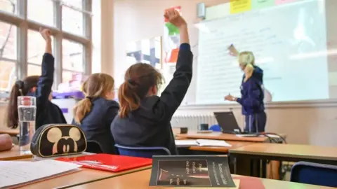 PA Media Children with their hands up in a classroom