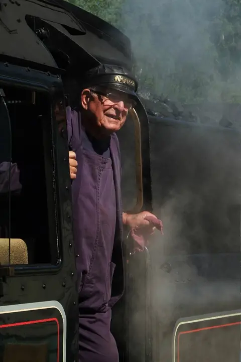 John Barry A man stands on the footplate of a steam locomotive