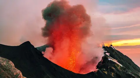 Generic stock photo for illustrative purposes only shows a cloud of smoke and lava coming out of a crater of a volcano around sunset, taken in Italy's Aeolian Islands