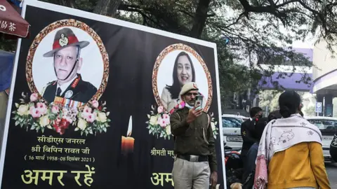 Getty Images A Delhi Police personnel takes a selfie in front of the poster of The Chief of Defense staff (CDS) during the funeral procession. General Bipin Rawat, his wife Madhulika and 11 other armed forces personnel lost their lives in an Indian Air force helicopter Mi-17V5 crash in Coonoor, Tamil Nadu.