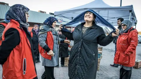 A group of women gather, with one tying on a headscarf.