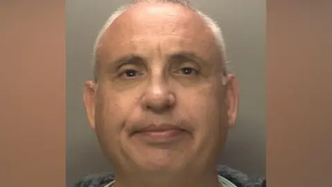 John Evans - a custody image of a clean-shaven man with short grey hair against a grey background.