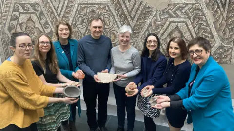 A group of people standing in a semi-circle while holding Roman artefacts