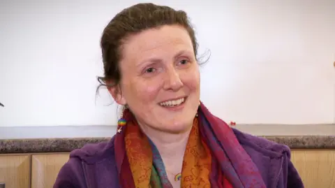 Nicola Smith - a woman wearing a purple jacket and as multi coloured top - smiles as she speaks to a person out of the picture