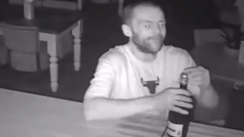 Man opens a bottle of Prosecco at a bar.