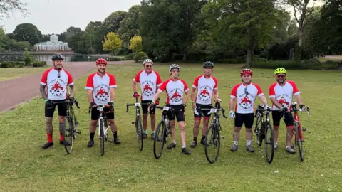 Wolverhampton Coronary Aftercare Support Group Seven people are on bikes on grass facing the camera. They are wearing cycling helmets and red and white tops including the words Have a Heart.