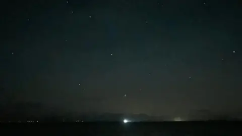 Millom Coastguard Rescue Team A dark stretch of sky with various bright white dots scattered across it. There is a light on the horizon.
