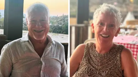 A smiling man and woman sat outside in the sun. 
