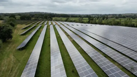 BBC A large solar farm showing many rows of panels in the British countryside 