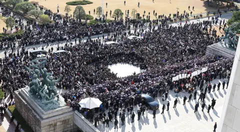 EPA A wide shot showing a mass of people gathered in the National Assembly square in front of parliamentary statues, in Seoul on Wednesday