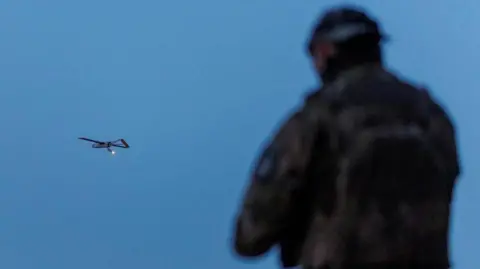 A Ukrainian soldier operating a drone, which is flying in the air in the background