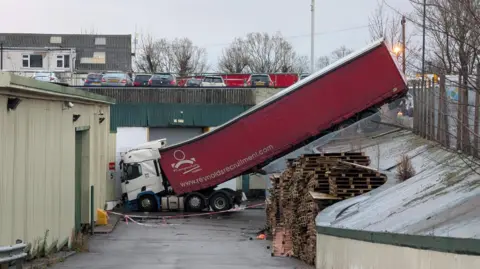 A red lorry that has become stuck after falling into an industrial estate