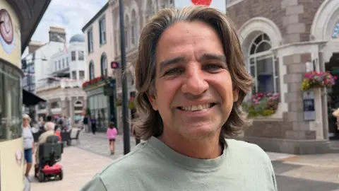 Ian Carr has long brown hair and is wearing a light green t-shirt