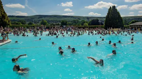 PA Media Dozens of people swimming and playing in the water at Ikley Lido.