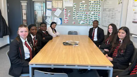 Students of different ages in uniform with blazers and ties looking at the camera.