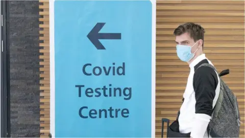 PA Media Man standing by a testing sign at Glasgow Airport