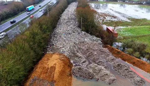 PA Media An aerial shot of the dumped waste, stretching out in a road-like line into the distance and surrounded on both sides by trees next to a motorway.