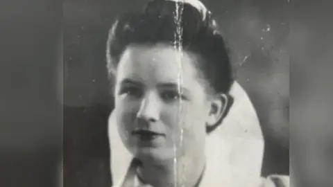 Supplied Black and white photograph showing a young woman with dark hair in a chignon and a serious expression. She is wearing a white collar, part of her nurse's uniform, which stands up behind the back of her neck.