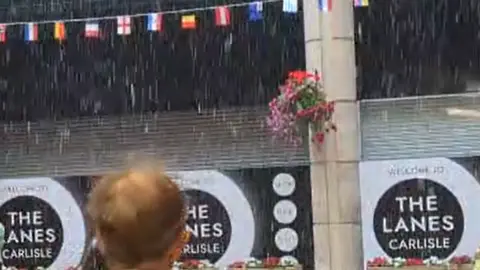 BBC/Ben Maeder A screenshot from a video shows water pouring into The Lanes, as shoppers watch on.