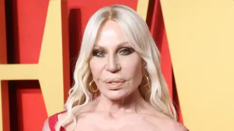 Getty Images Donatella Versace attends the 2024 Vanity Fair Oscar Party - close up of her face with a red and yellow backdrop.