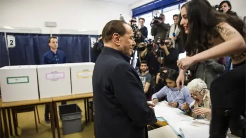 Getty Images Mr Berlusconi stands in front of press as a woman standing on a table, with slogans written on her topless torso