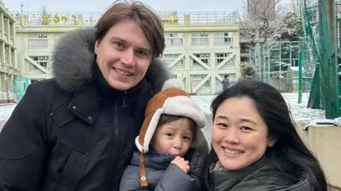 Chika Nakayama/BBC Rumi and Daniel Hayama smiling as Rumi hold their son.