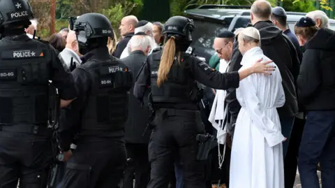People gather near the scene, after a report of an incident in which a car was driven at pedestrians and a stabbing attack, near a synagogue in north Manchester.