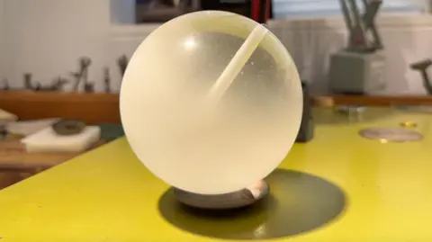 A while to translucent orb on a small wooden round base, sitting on a yellow-topped counter.