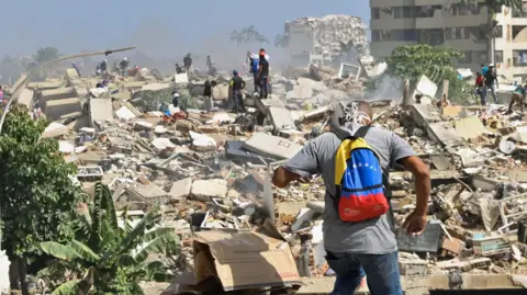 A man with a Venezuelan flag-themed backpack walks amid rubble of collapsed buildings after earthquakes hit the country.