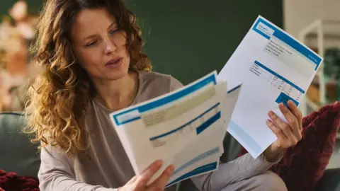 Woman with long hair looks at energy bill while sitting on a sofa. 