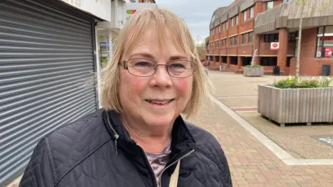 A woman is standing in the town centre smiling - Lyn Mader is a volunteer litter picker. 