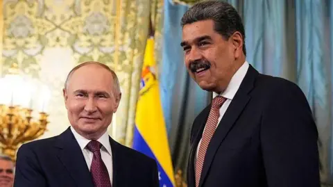 Getty Images Russian President Vladimir Putin in a dark suit with a burgundy tie patterned with white dots shakes hands with Venezuelan President Nicolás Maduro, who wears a dark suit and an orange tie with white dots
