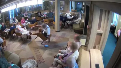 MAIB/Saga Cruises A passenger is tipped backwards in his chair by the ship's movement in The Club on board the ship. Other passengers are sitting nearby.